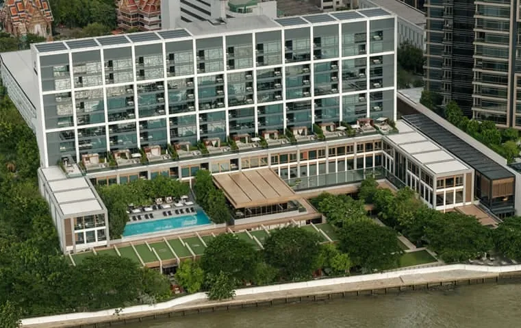 Capella Bangkok's low-rise riverfront facade and infinity pool along the Chao Phraya River at dusk