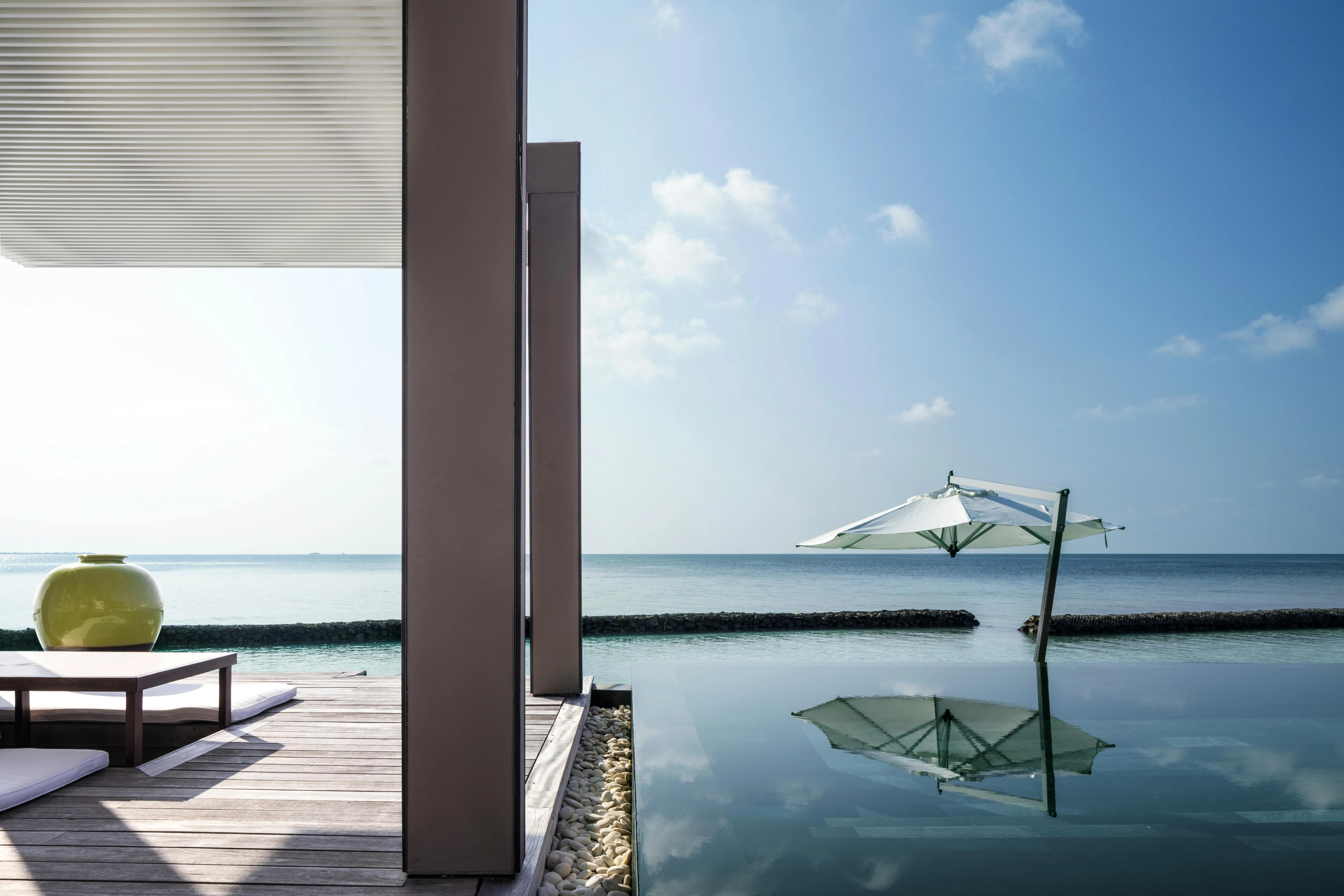 An overwater villa at Cheval Blanc Randheli at dusk, its cathedral-height roofline silhouetted against the Noonu Atoll lagoon