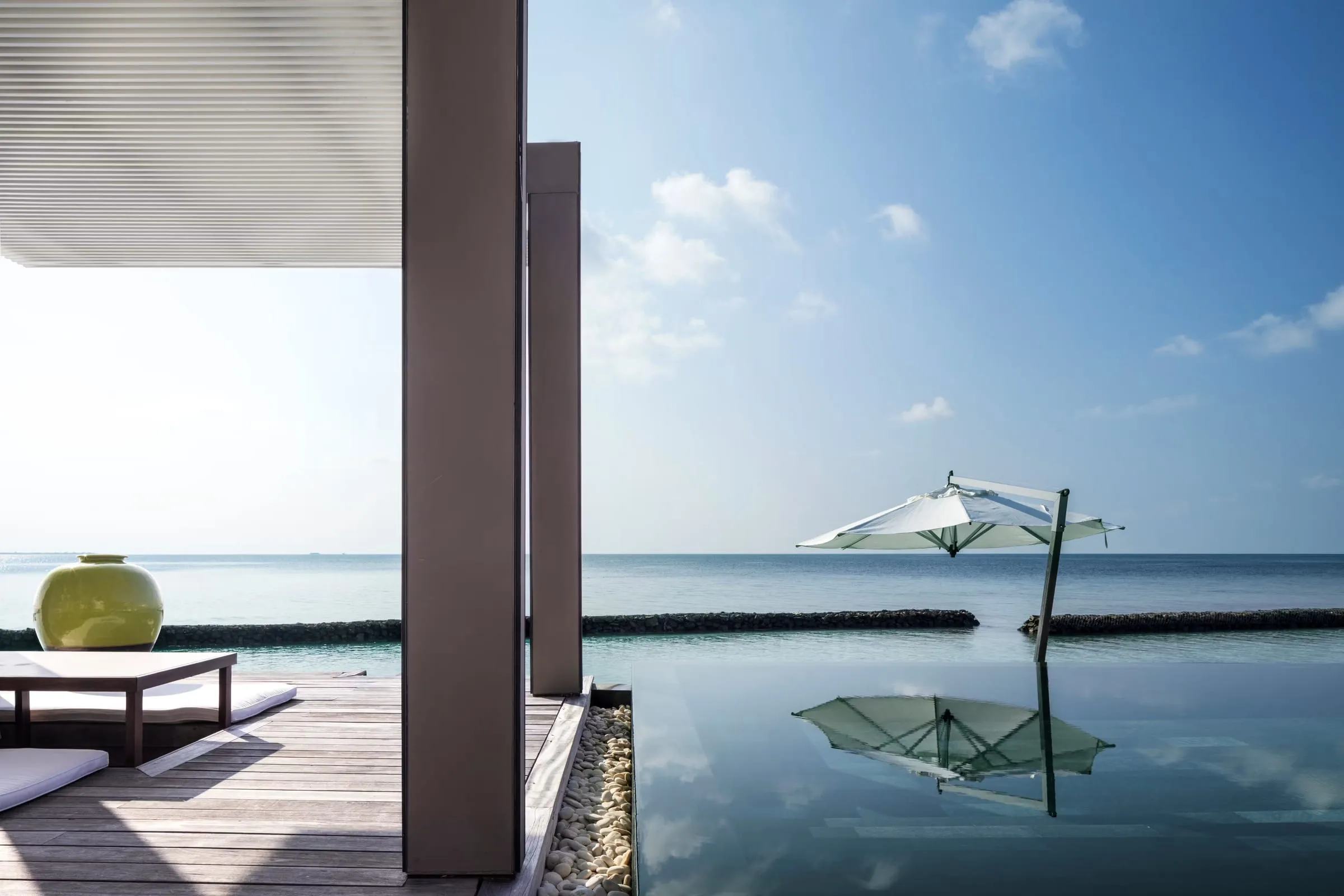 An overwater villa at Cheval Blanc Randheli at dusk, its cathedral-height roofline silhouetted against the Noonu Atoll lagoon