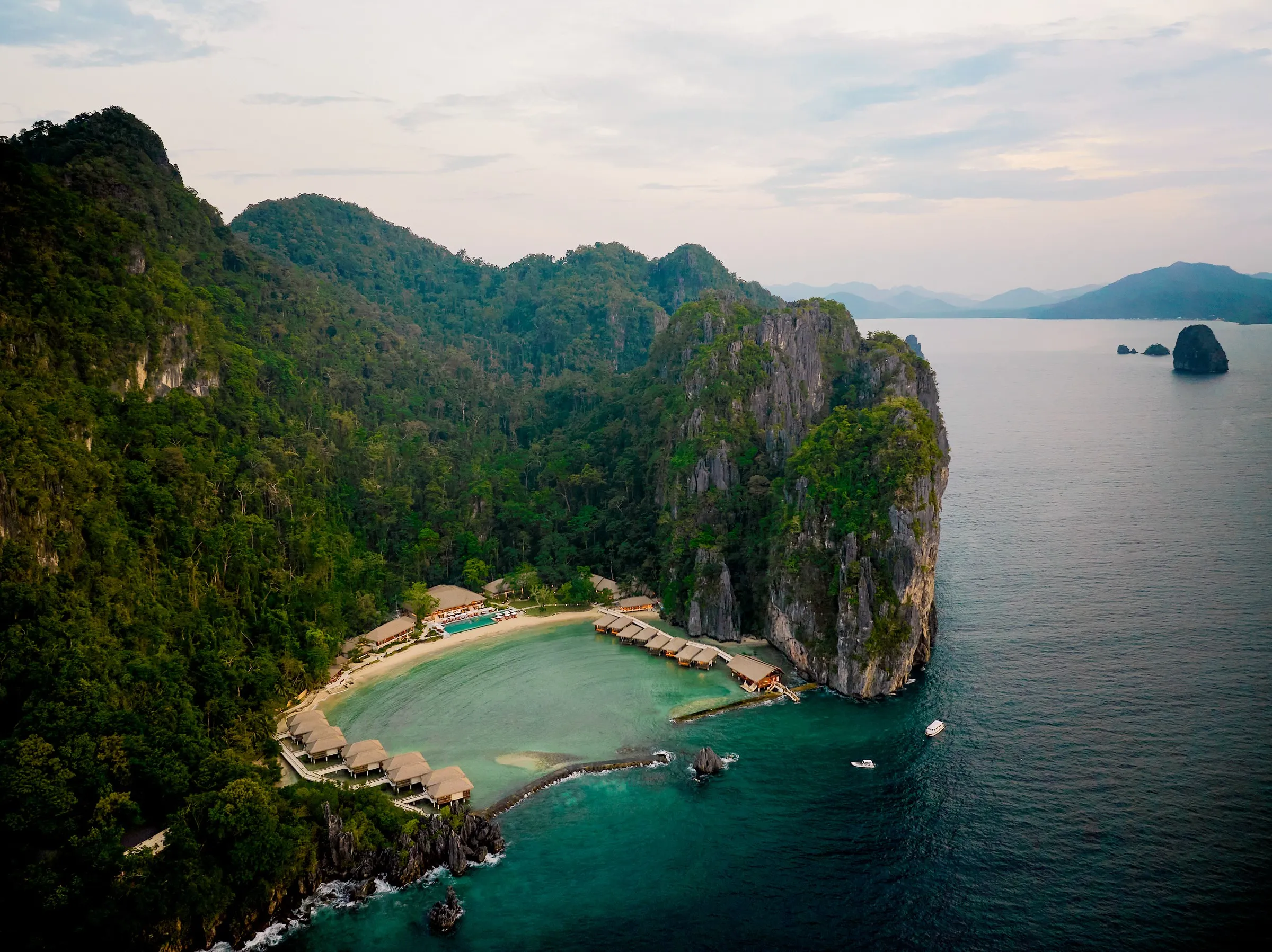 Water cottages on stilts at Lagen Island Resort framed by limestone cliffs and dense forest canopy in Bacuit Bay