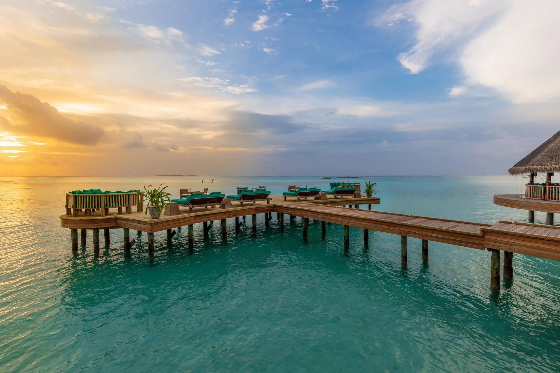 Open-sided villa interior with driftwood furniture, a hanging daybed and views straight out to the Indian Ocean