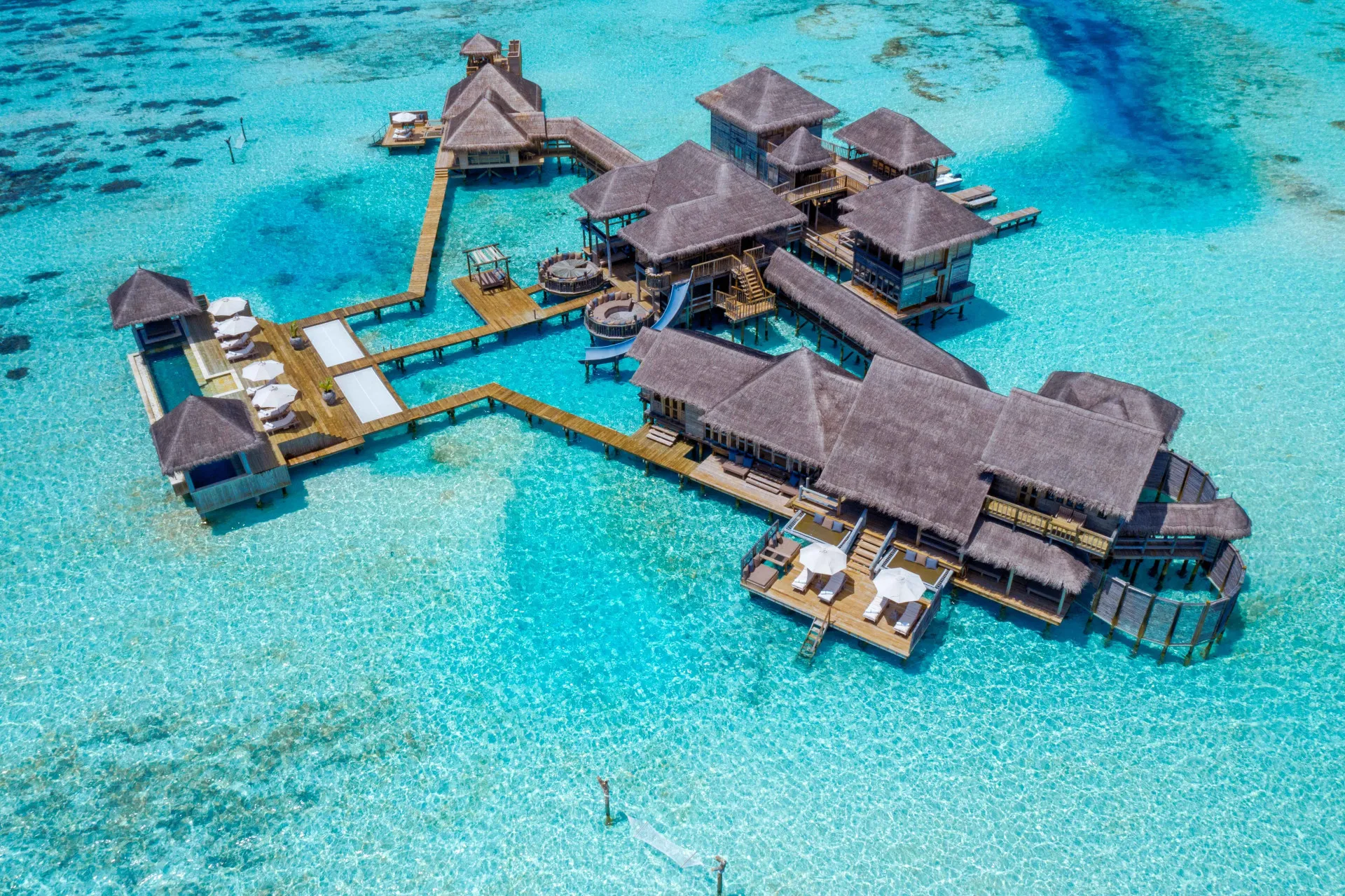 Overwater dining table set for two at dusk with lanterns above a calm lagoon