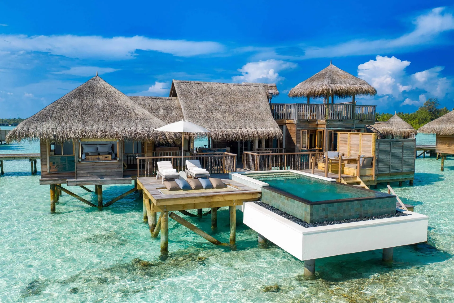 An overwater villa at Gili Lankanfushi with a thatched roof and driftwood deck extending over a turquoise lagoon in North Male Atoll