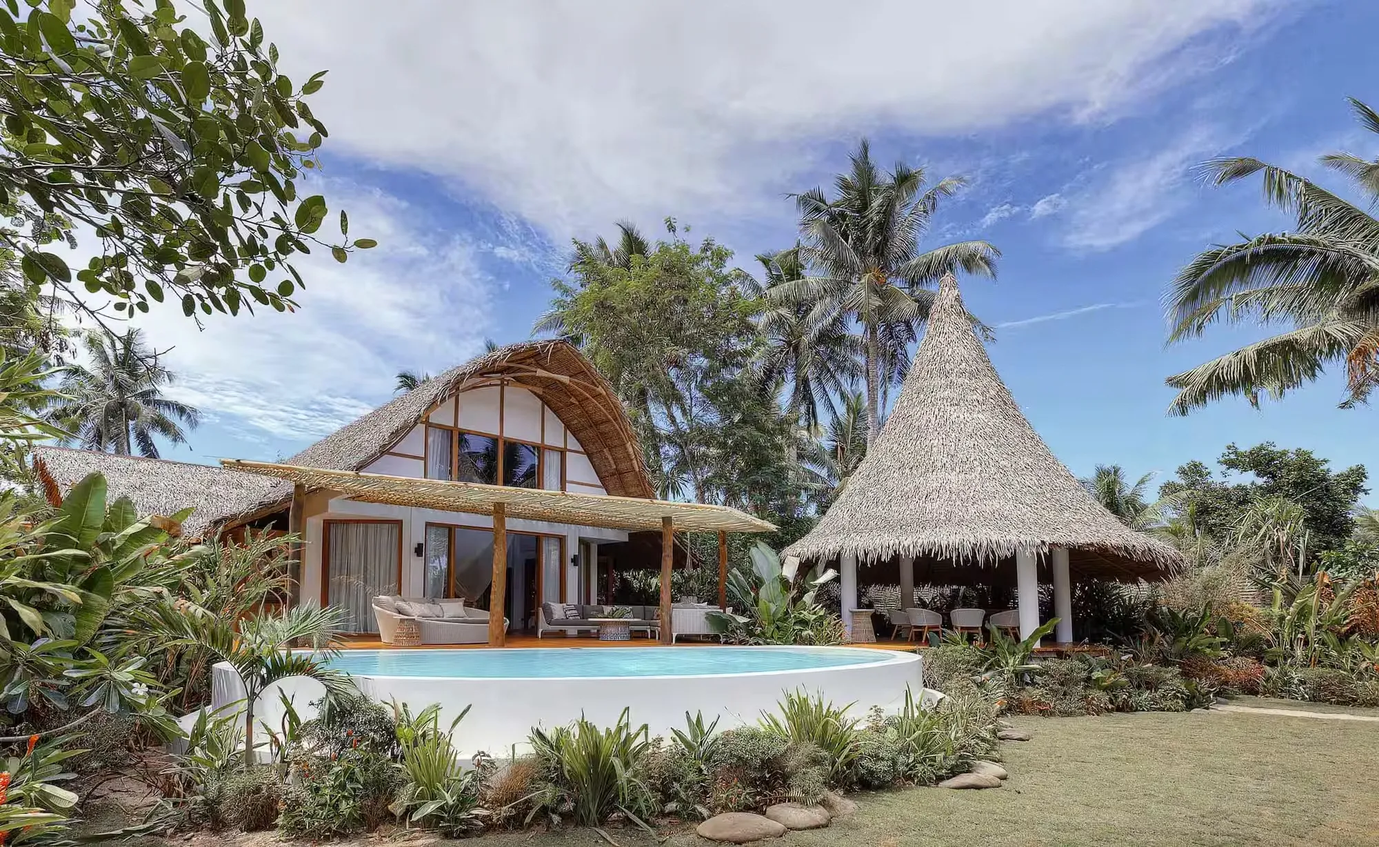 A thatch-roofed villa at Nay Palad Hideaway set among palm trees on Siargao Island, with a private pool facing the tree line