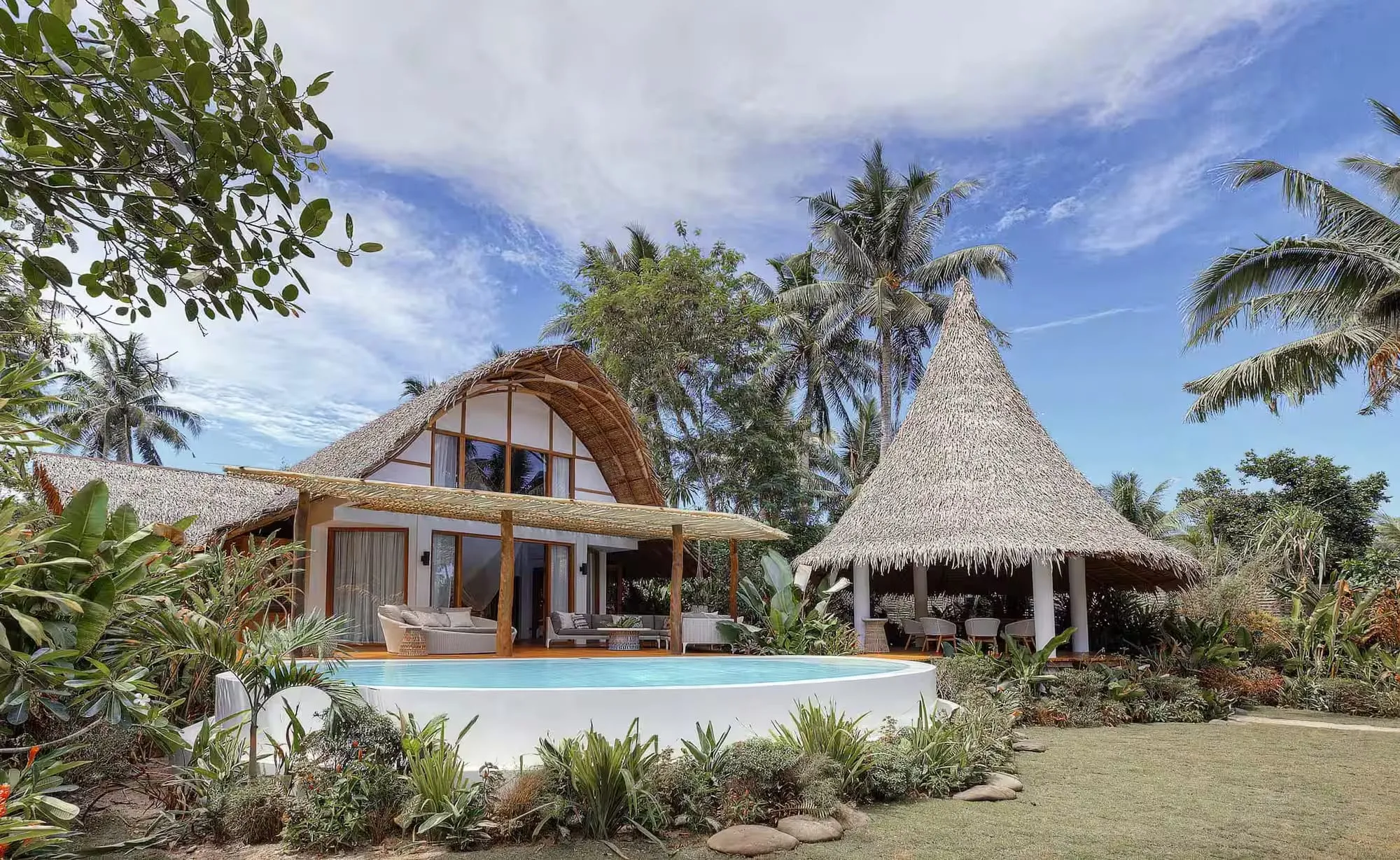 A thatch-roofed villa at Nay Palad Hideaway set among palm trees on Siargao Island, with a private pool facing the tree line
