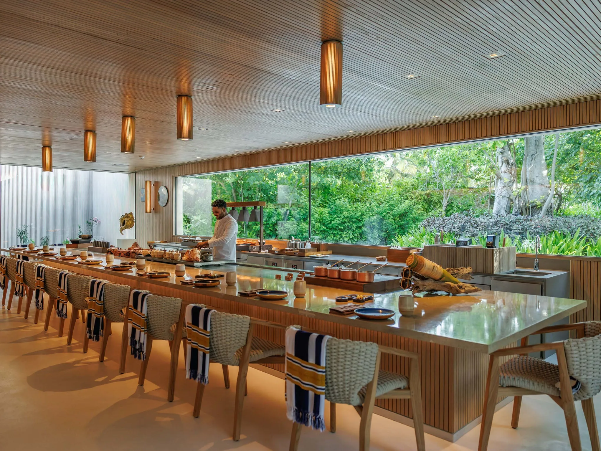 Interior of a Patina Maldives villa with rattan, wood and stone furnishings and a floor-to-ceiling sliding glass wall