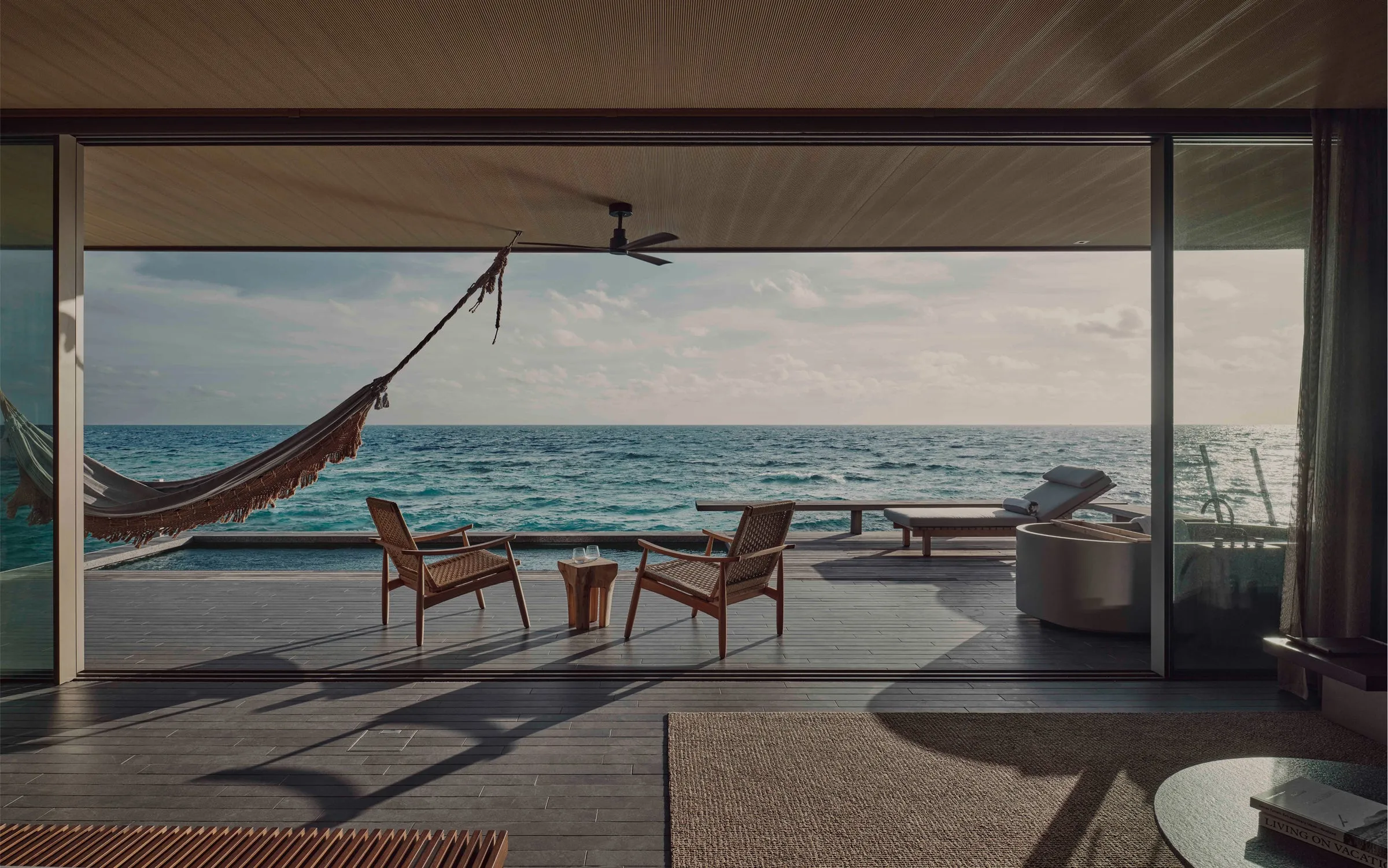 A low-slung, canopy-height villa at Patina Maldives with floor-to-ceiling sliding glass walls opening onto a private pool and the lagoon beyond