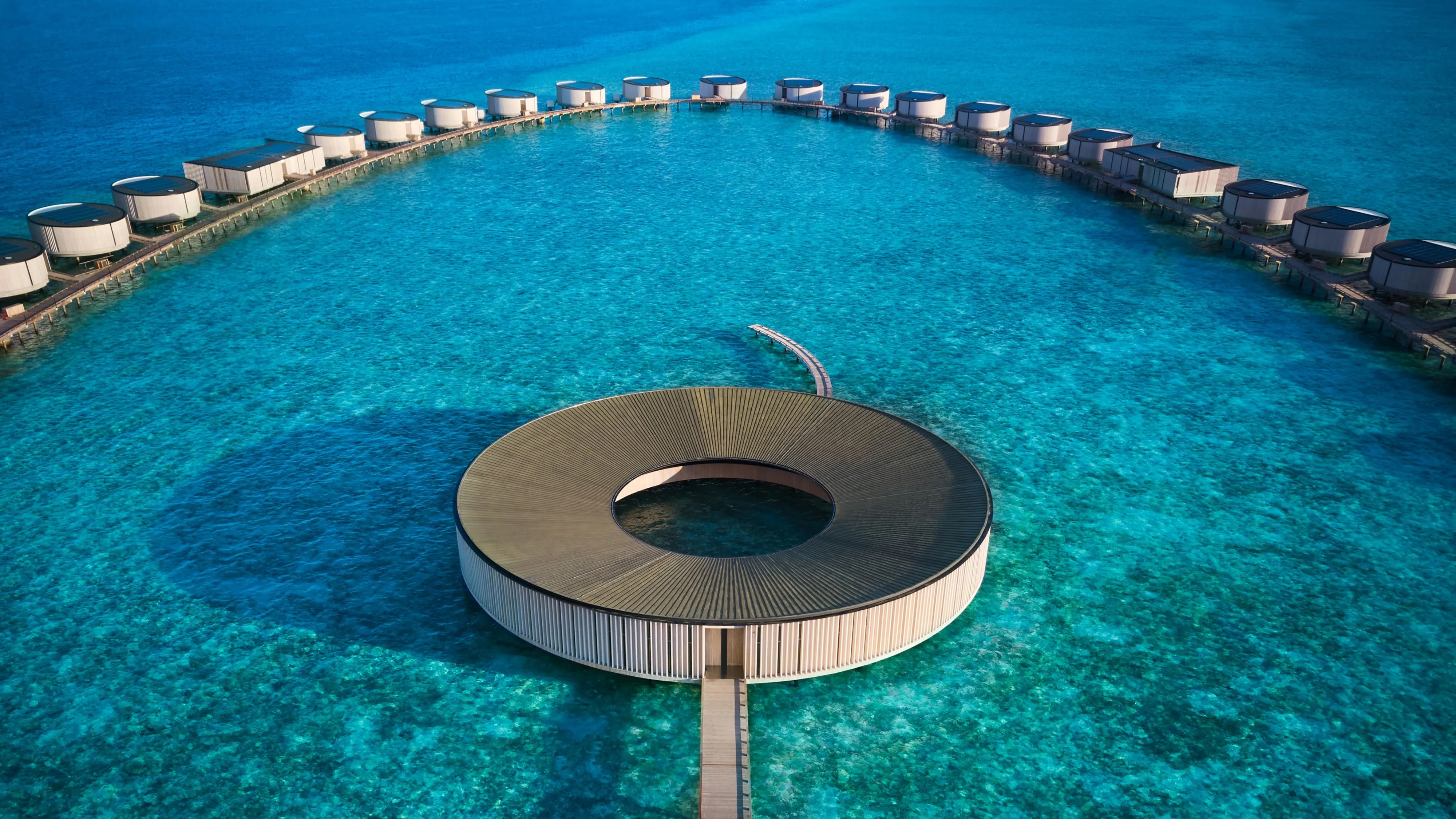 The circular overwater spa structure at sunset, ringed by still lagoon water