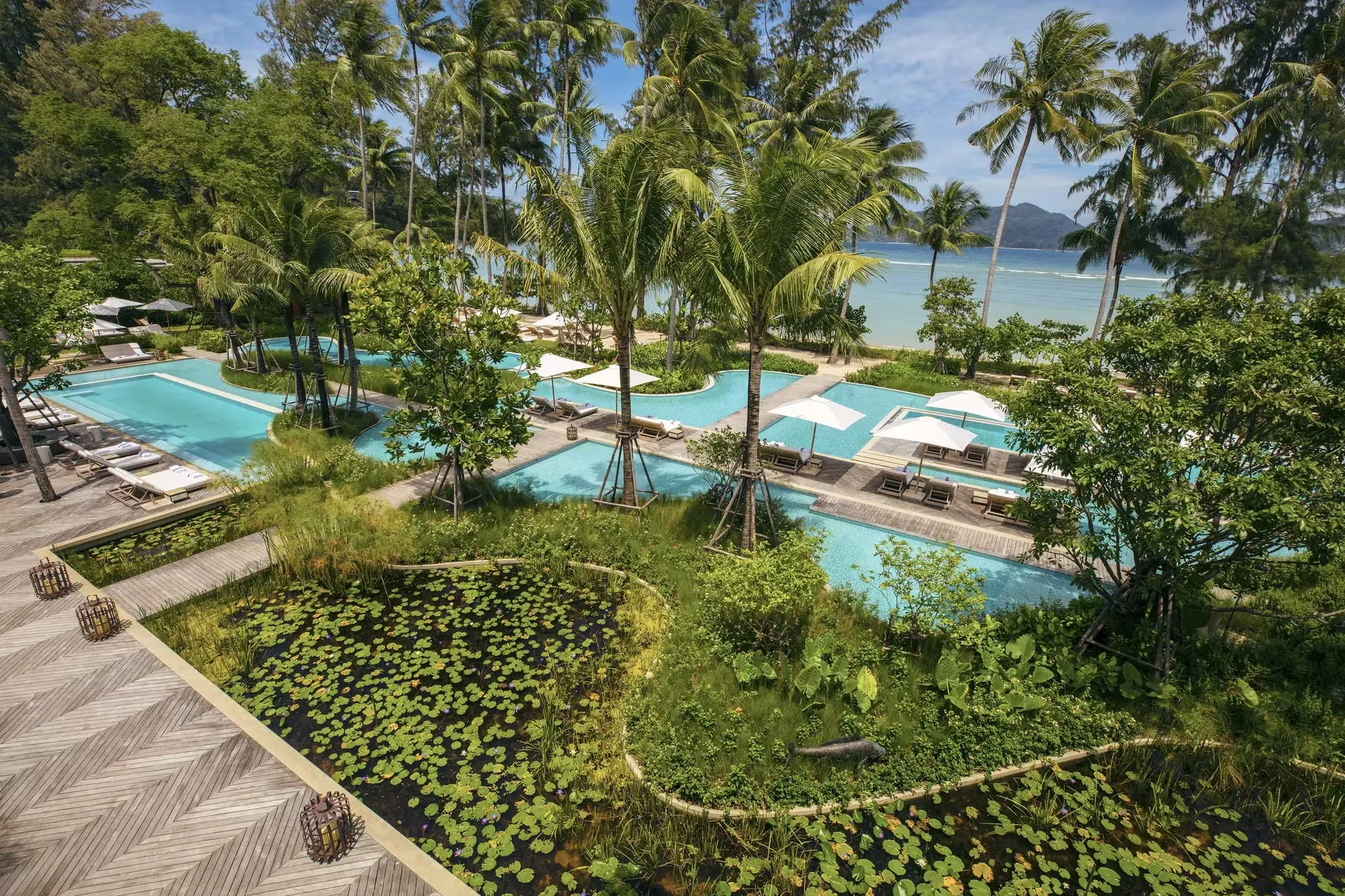 Tiered pool pavilions of Rosewood Phuket descending a forested hillside toward the Andaman Sea at Emerald Bay