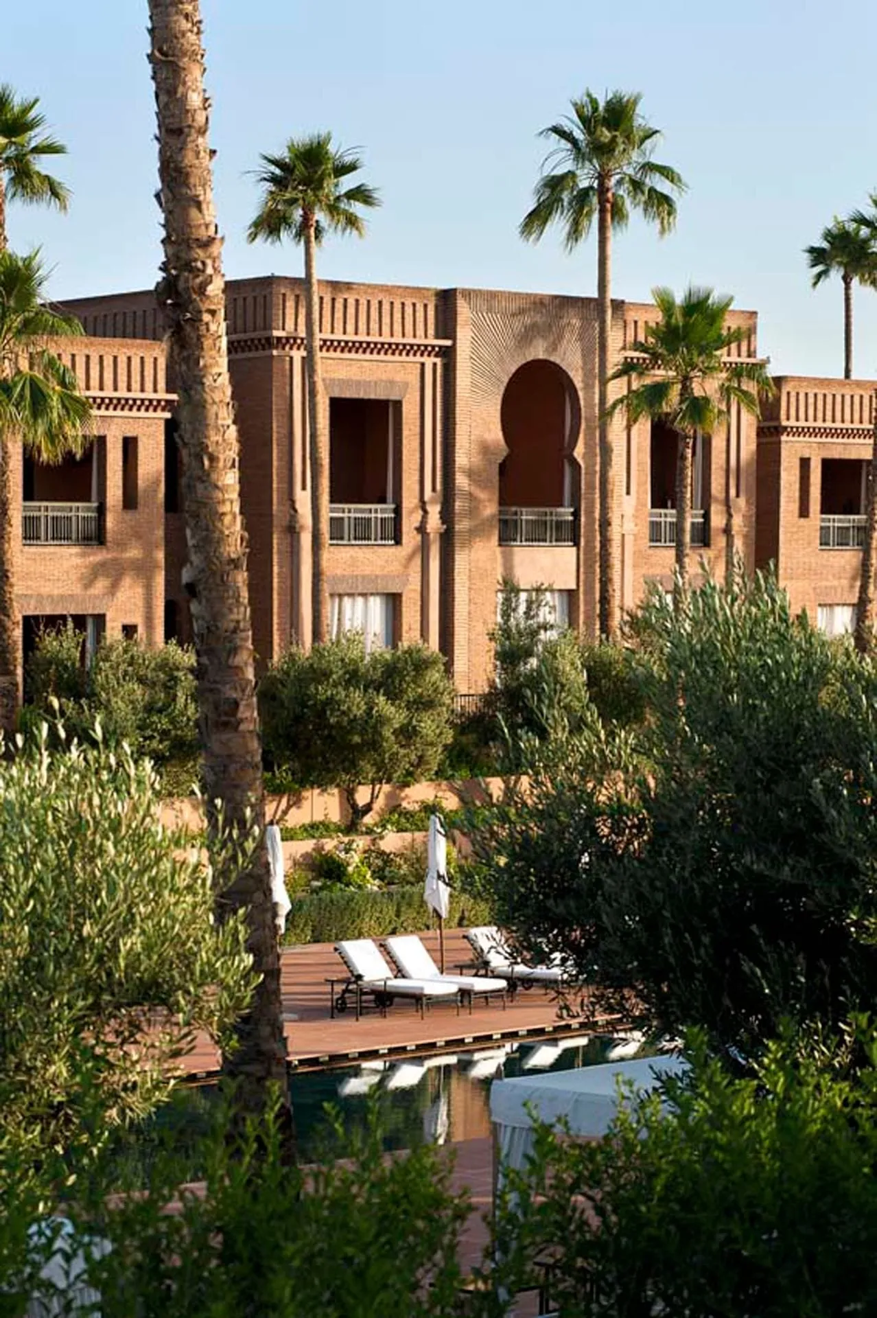 The Arab-Moorish palace of Selman Marrakech at dusk, with Arabian horses grazing in paddocks against the Atlas Mountains