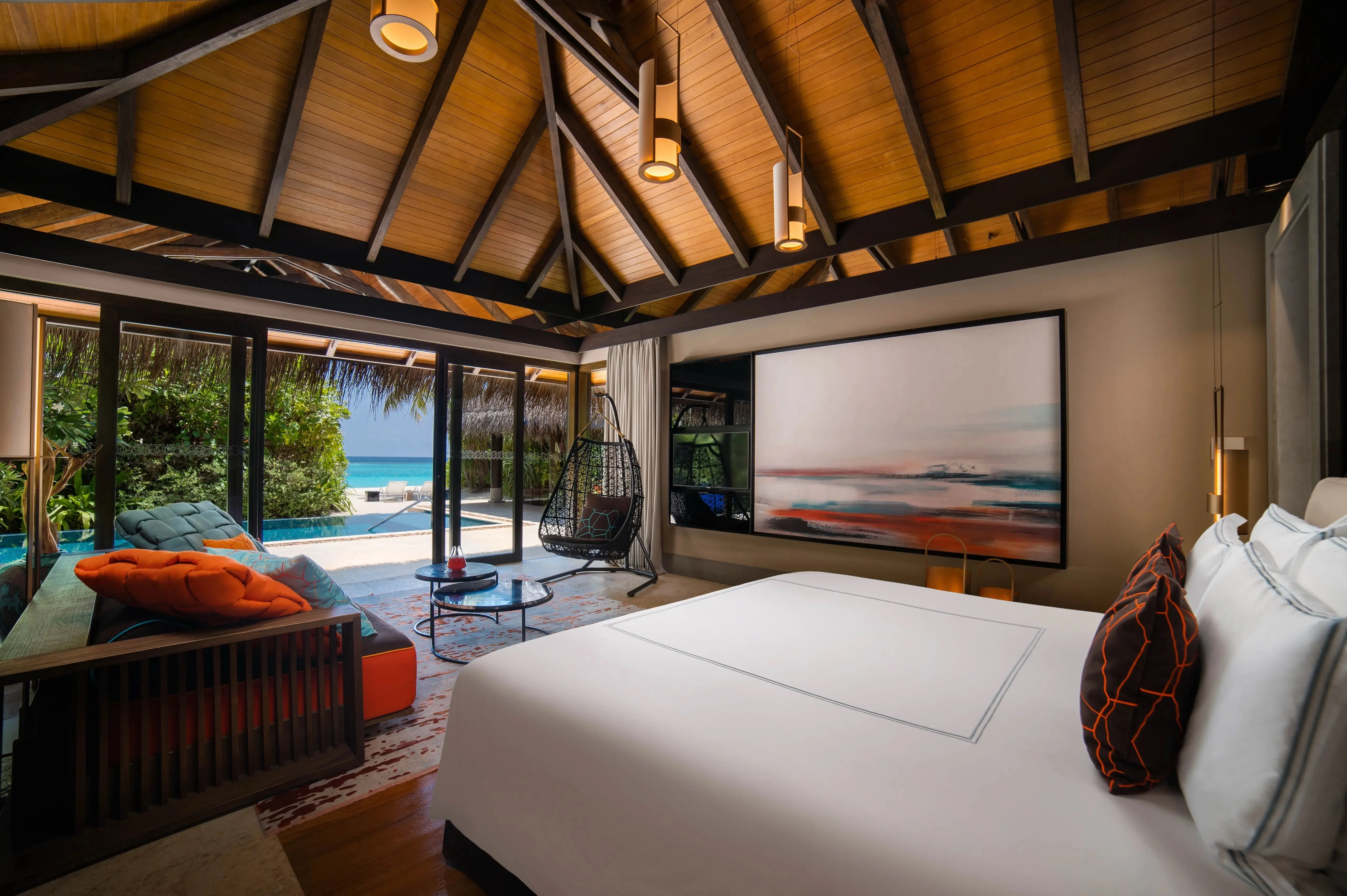 Interior of a Velaa water villa with natural timber, a freestanding tub and glass doors opening to a private deck over the lagoon