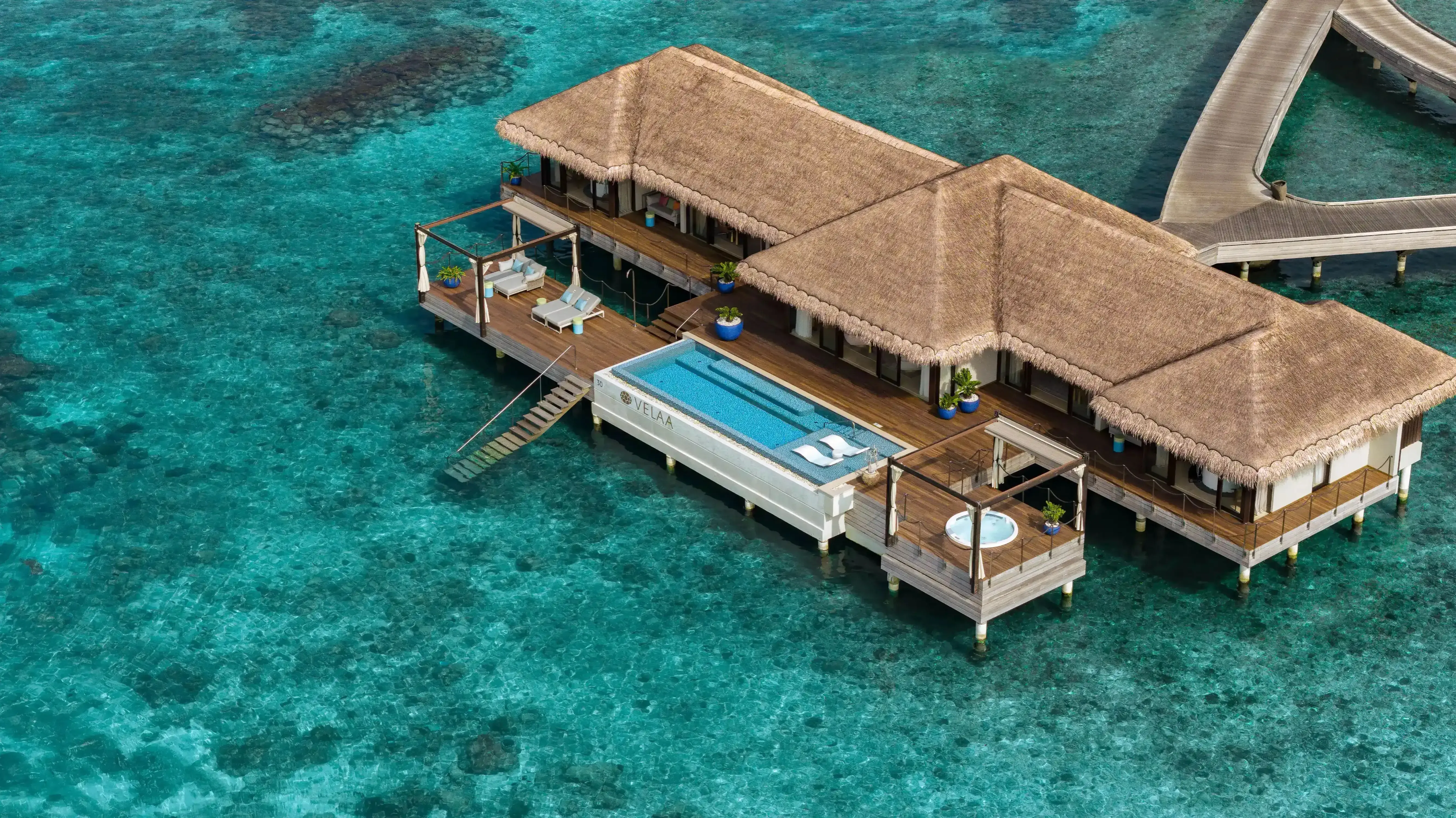 Overwater villas at Velaa Private Island with thatched roofs stepping across a turquoise lagoon in Noonu Atoll, Maldives