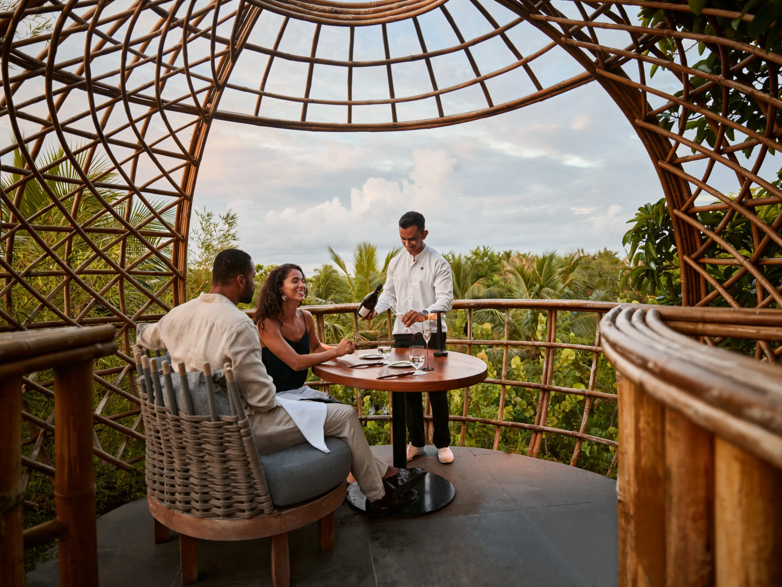 Bamboo dining pods set among treetop greenery at dusk, lit from within