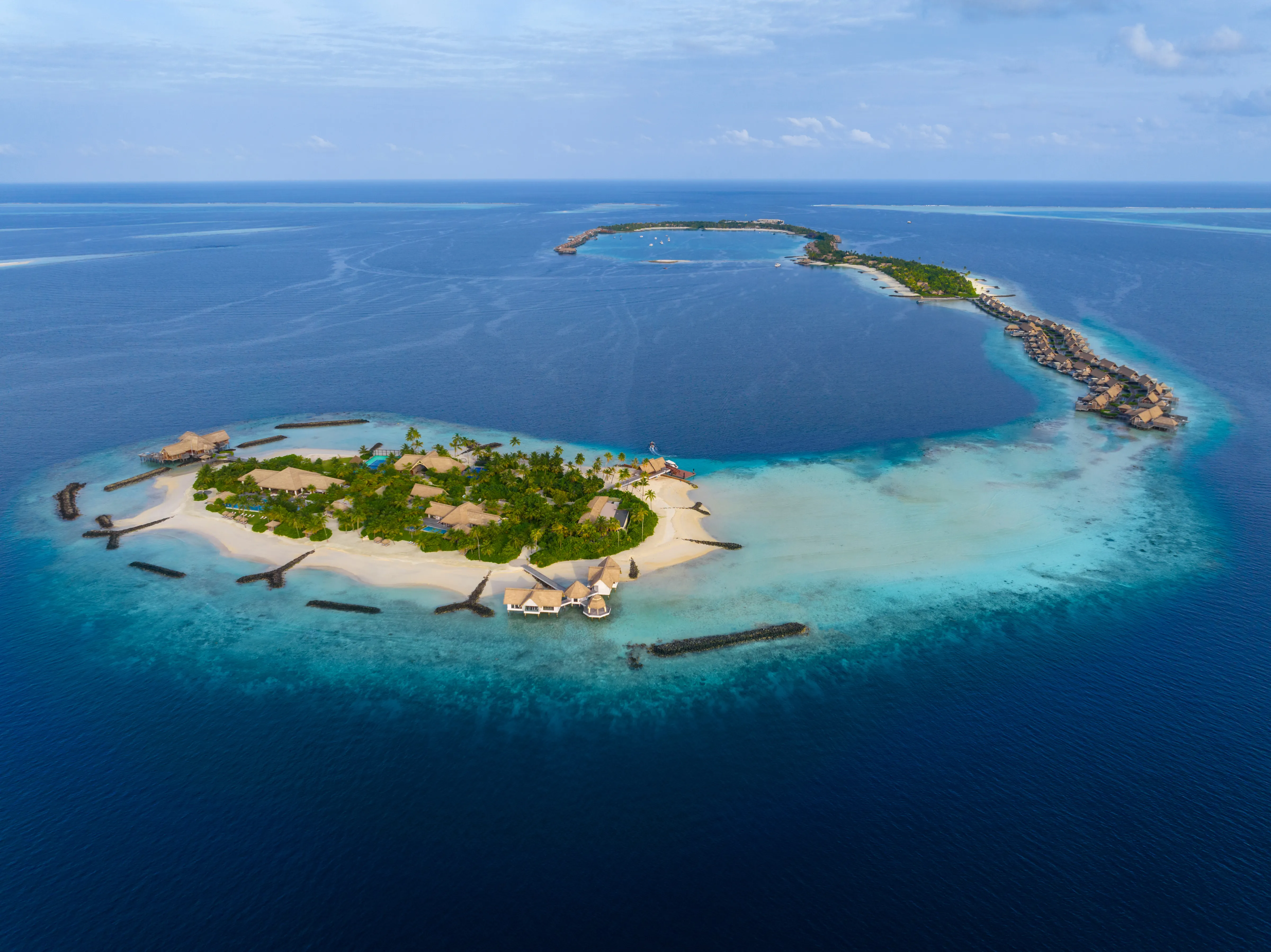 Overwater villas on stilts above a pale turquoise lagoon at Waldorf Astoria Maldives Ithaafushi, with wooden walkways connecting them across the water